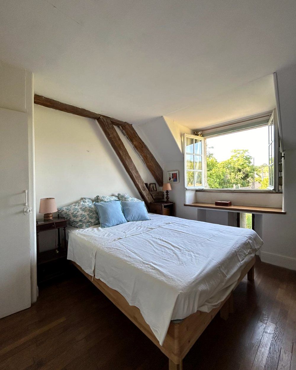 Une chambre double, des coussins bleus et une fenêtre ouverte sur les arbres