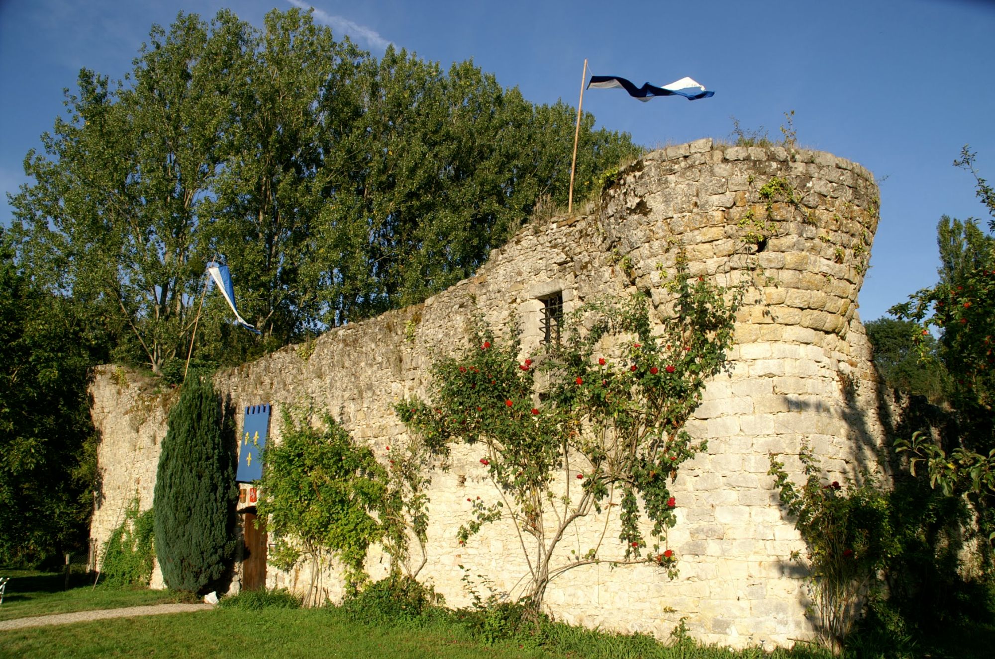 La muraille du Fort de Challeau, ses roses, sa porte de bois et sa bannière fleurdelisée